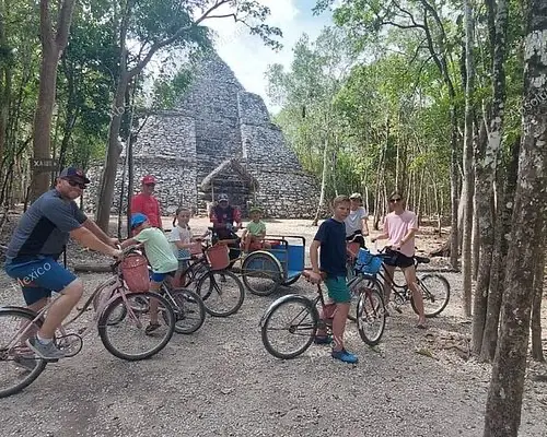 Cyclists exploring the ruins of Coba with Nohoch Mul pyramid in the distance, a must-do day trip from Cancun

